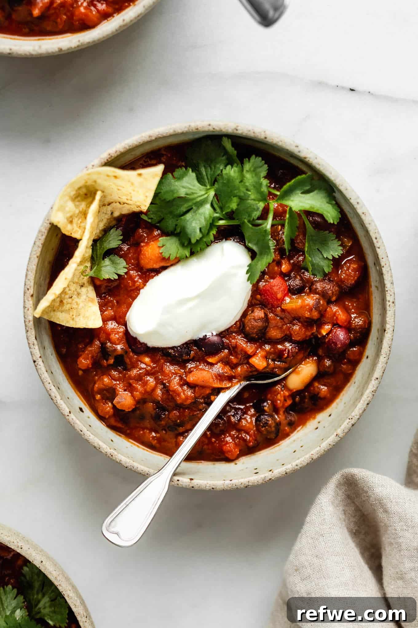 A close-up of a rustic bowl filled with hearty Instant Pot vegan chili, featuring a spoon ready for a taste.