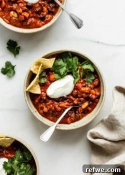 Three bowls of vegan chili topped with vegan sour creme, cilantro and tortilla chips