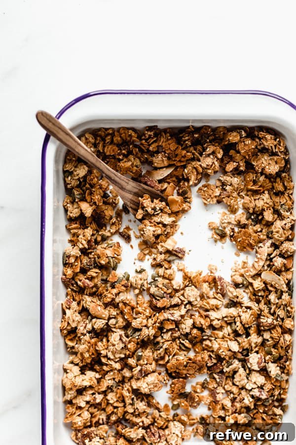 Citrus Cardamom Tahini Granola Crunch 3 A white enamel baking pan filled with golden-brown, baked tahini granola, showing its cluster formation.