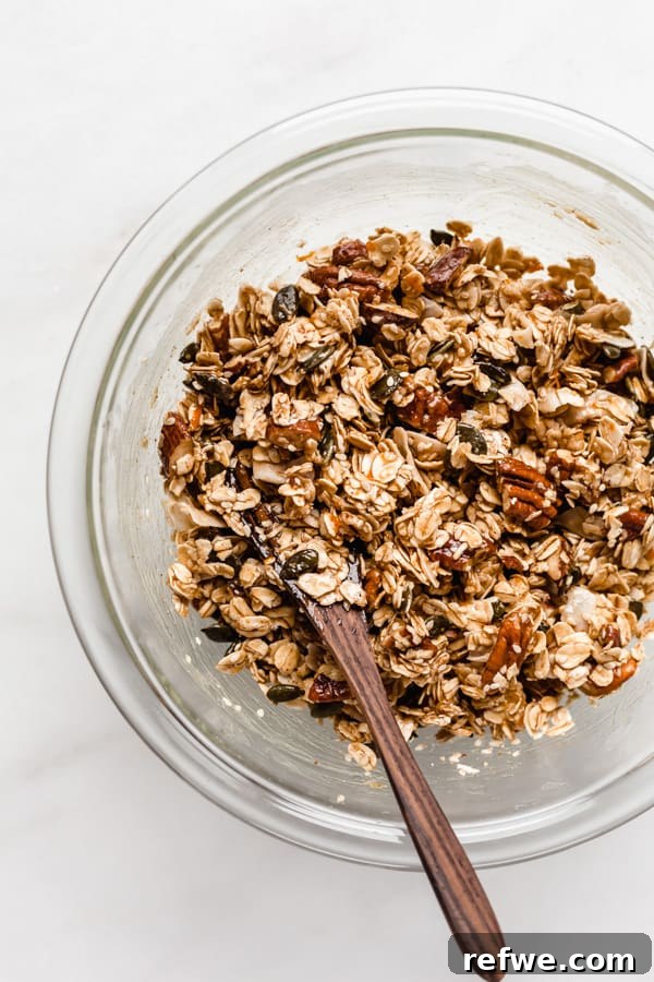 Citrus Cardamom Tahini Granola Crunch 6 A clear mixing bowl holding un-baked tahini granola, perfectly coated and ready to be spread onto a baking sheet.