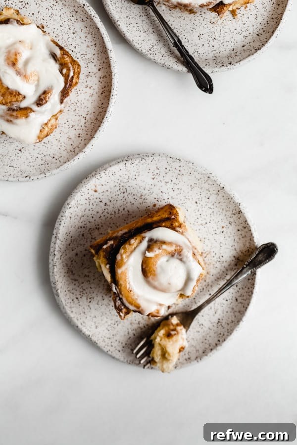 Cozy Vegan Pumpkin Spice Cinnamon Buns 6 Three white speckled plates, each holding a delicious vegan pumpkin spice cinnamon roll, showcasing their inviting golden color and gooey texture.