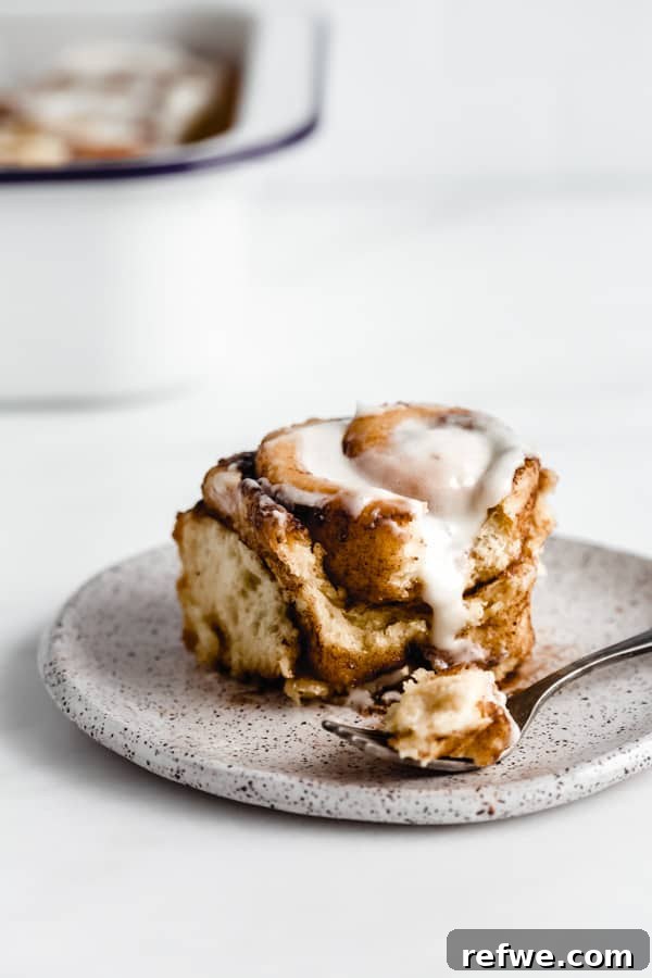 Cozy Vegan Pumpkin Spice Cinnamon Buns 7 A delectable vegan pumpkin spice cinnamon roll on a white plate with a fork, showing a bite taken out, revealing the soft, gooey interior.