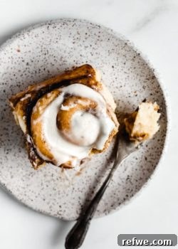 A cinnamon roll on a white speckled plate topped with cream cheese frosting