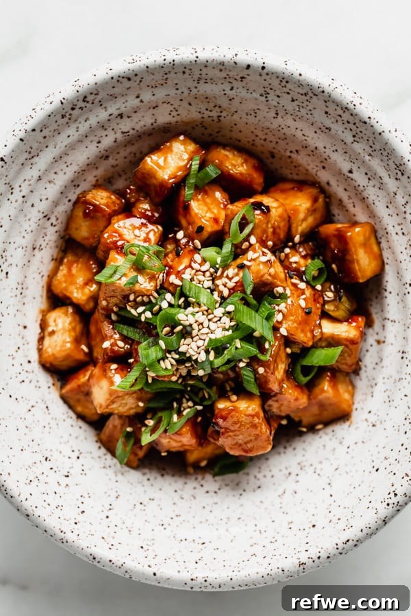 A vibrant bowl of General Tso Tofu, generously garnished with fresh green onions and sesame seeds, ready to eat.
