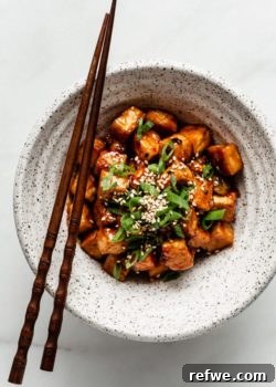 General Tso Tofu in a speckled ceramic bowl with wooden chopsticks on the side, ready to eat.
