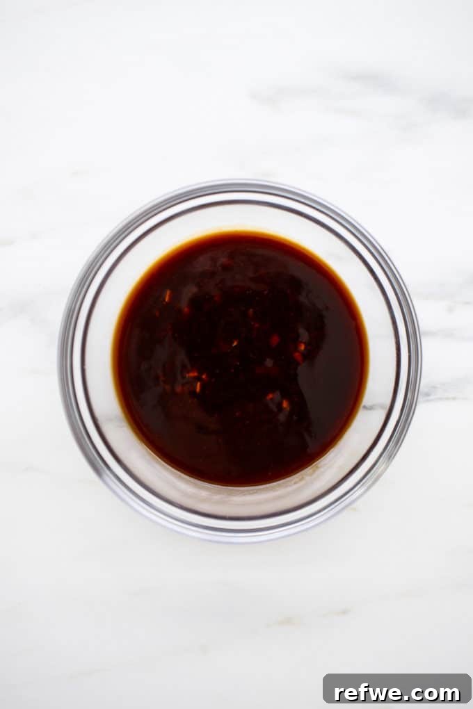 A small bowl filled with the rich, amber-colored General Tso's sauce, ready to be added to the tofu.
