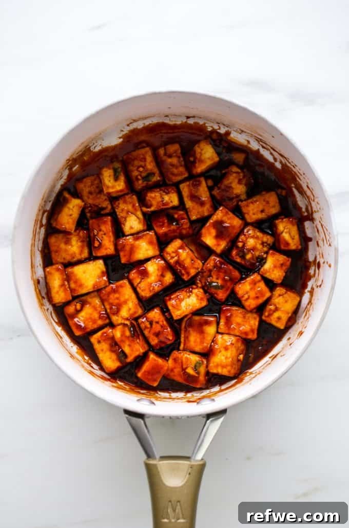 General Tso's tofu actively being coated in the rich, glossy sauce in a white pan.