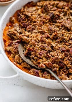 A generous serving of vegan sweet potato casserole with a pecan crumble topping, scooped with a spoon.