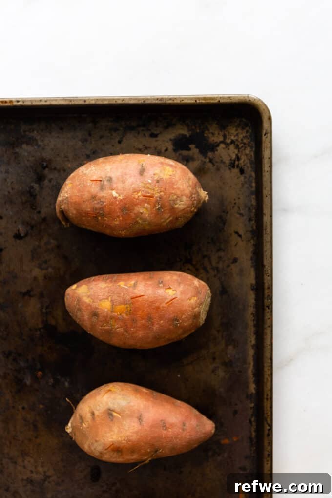 Three sweet potatoes laid out on a baking sheet, ready for roasting.