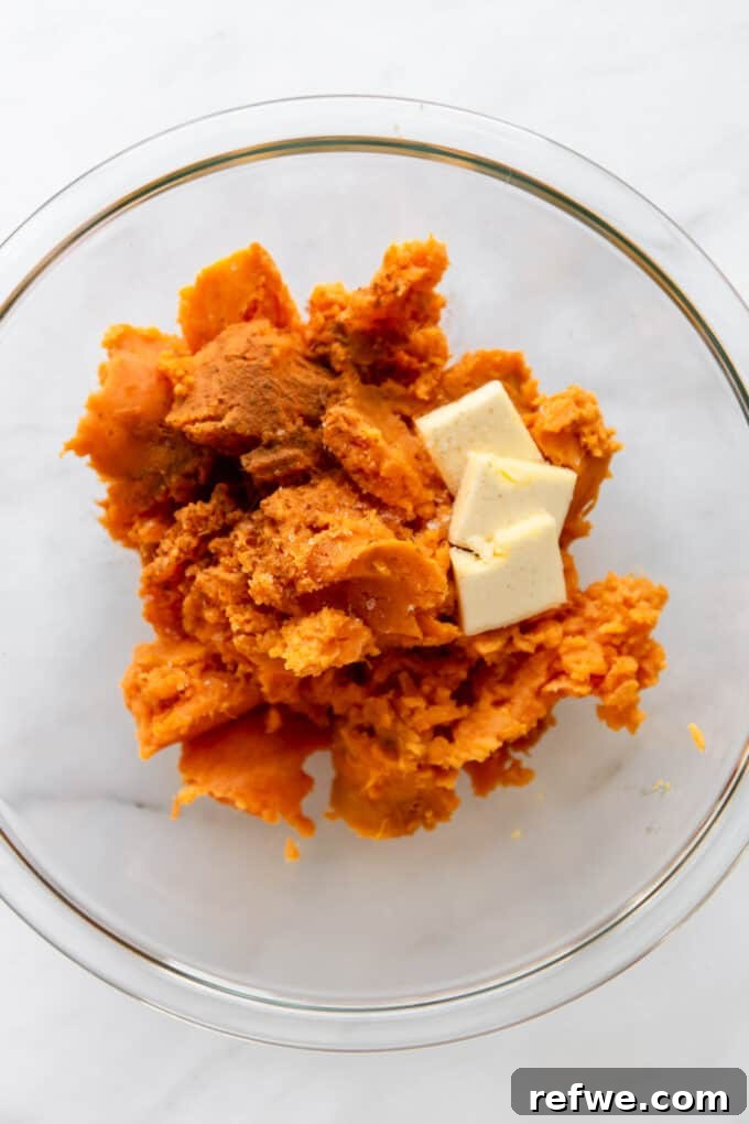 Sweet potato flesh, vegan butter, and cinnamon in a clear mixing bowl before mashing.
