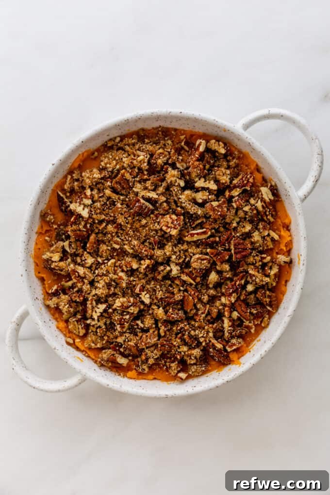 Vegan sweet potato casserole in a round dish, topped with pecan crumble and ready for baking.