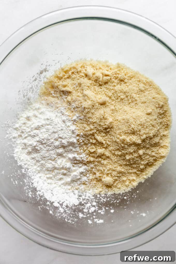 Almond flour, cornstarch, and a pinch of salt are precisely measured and gently mixed in a clear glass bowl, forming the foundational dry ingredients for the crust.