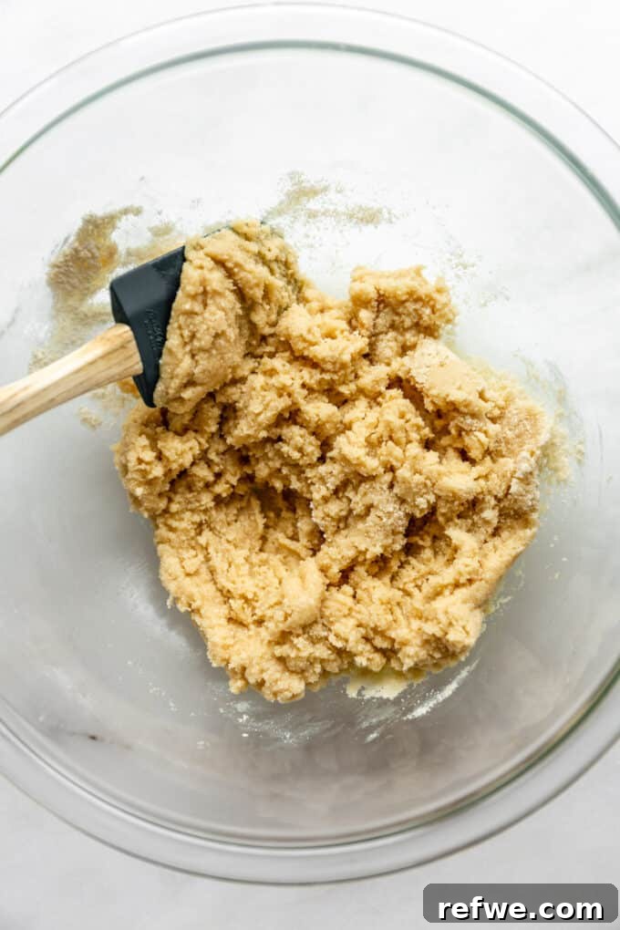 The almond flour mixture is transformed into a soft, cohesive dough after melted coconut oil, maple syrup, and vanilla extract are folded in, resting in a mixing bowl.