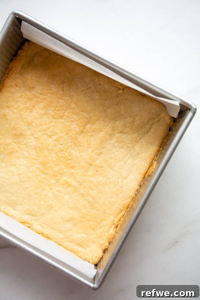 The baked almond flour crust, golden brown and perfectly set, rests in an 8x8 inch pan after pre-baking, cooling down before the pecan topping is added.