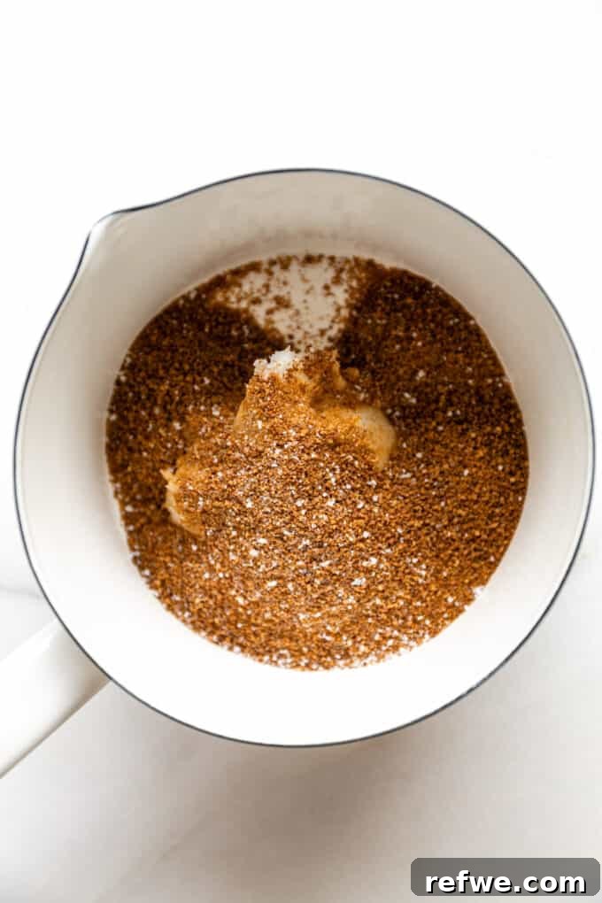 Melted coconut sugar, coconut oil, salt, and vanilla extract simmering gently in a small saucepan on the stovetop, creating a rich, bubbling caramel base for the pecan filling.