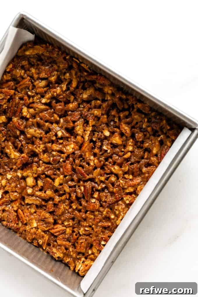 The freshly baked pecan pie bars, now boasting a rich golden-brown topping, are cooling in an 8x8 inch pan, ready to be sliced after setting.