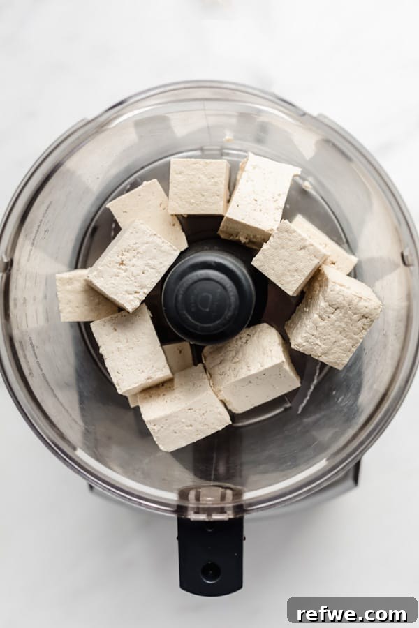 Easy Chipotle Copycat Tofu Sofritas 3 Large cubes of extra-firm tofu ready for crumbling in a food processor, highlighting the initial preparation step for optimal texture.