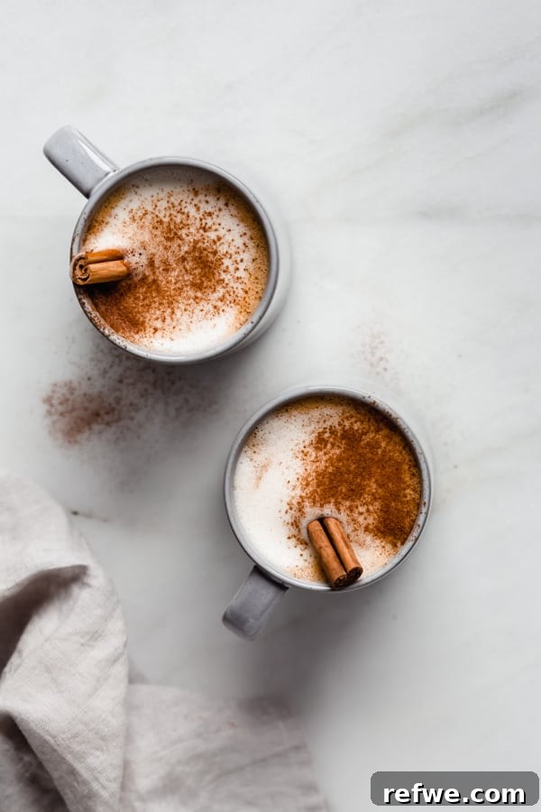 Warm Vegan Pumpkin Spice Delight 3 Two cozy blue mugs of vegan pumpkin spice latte, each adorned with a cinnamon stick, sit invitingly on a wooden surface, ready to be enjoyed.