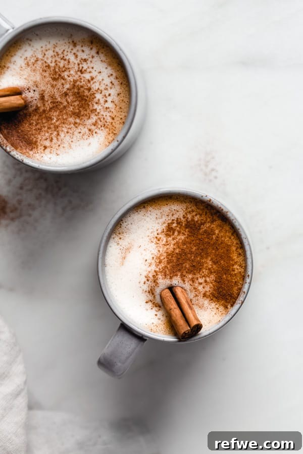 Warm Vegan Pumpkin Spice Delight 4 Two aesthetically pleasing blue mugs of vegan pumpkin spice latte, generously topped with cinnamon powder and cinnamon sticks, presented on a light background.