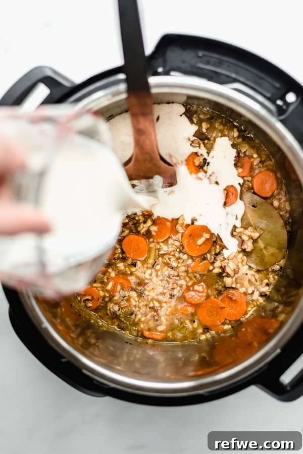 Creamy Instant Pot Wild Rice Comfort 7 Creamy cashew blend being poured into the Instant Pot, mixing with the cooked wild rice soup.