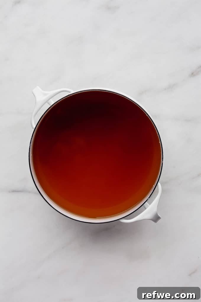 Aromatic Vegan Pho 5 A pristine white pot holds a clear, golden vegan pho broth, hinting at the delicate balance of spices and savory notes ready to be served.