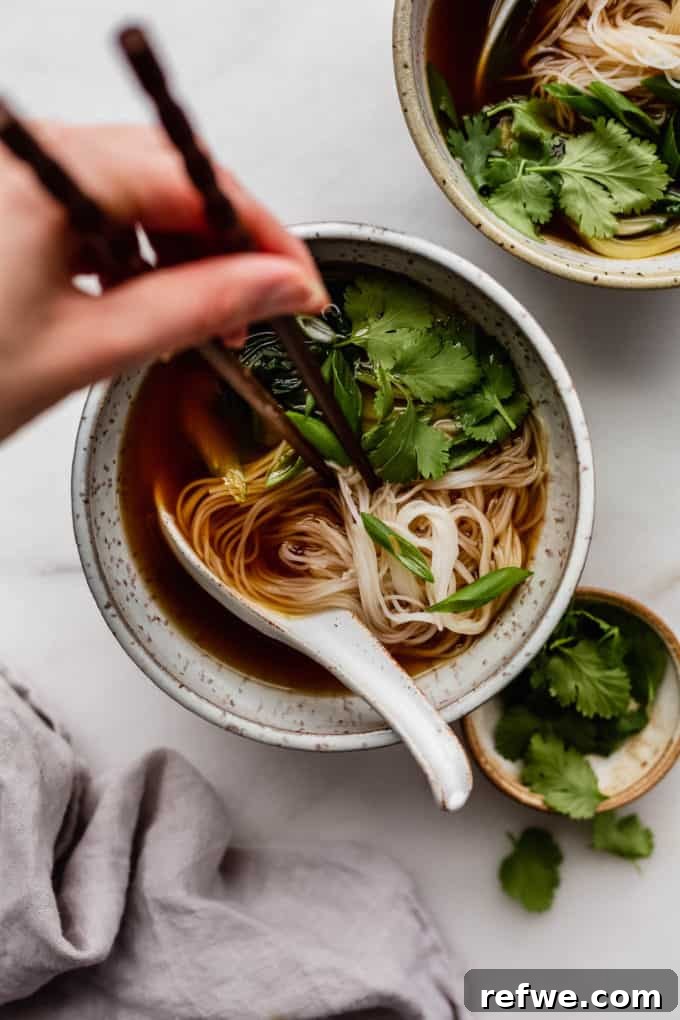 Aromatic Vegan Pho 8 A beautifully composed bowl of vegan pho, featuring delicate noodles submerged in rich broth, topped with fresh greens, and accompanied by chopsticks, ready to be enjoyed.
