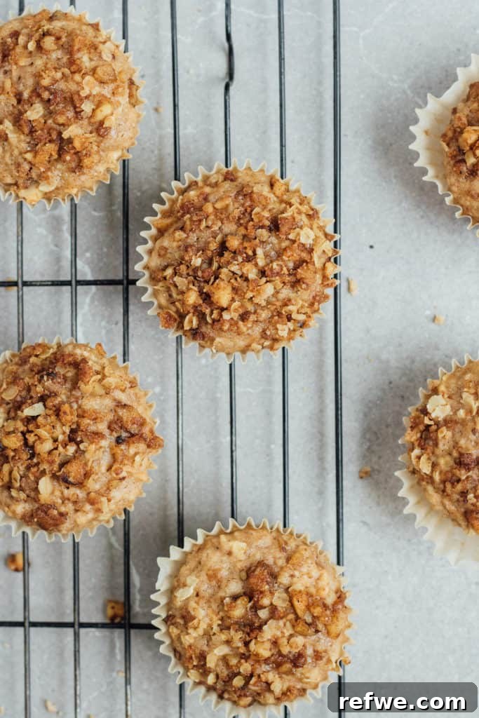 Comforting Vegan Apple Crumb Muffins 4 Three vegan apple crumb muffins stacked on a wooden board, showcasing their inviting texture.