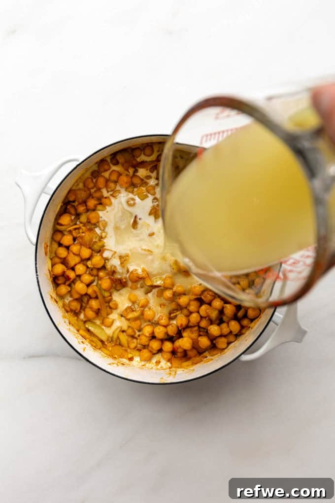 Creamy Coconut Chickpea Stew 7 Vegetable broth being poured into a pot of chickpeas and curry spices.