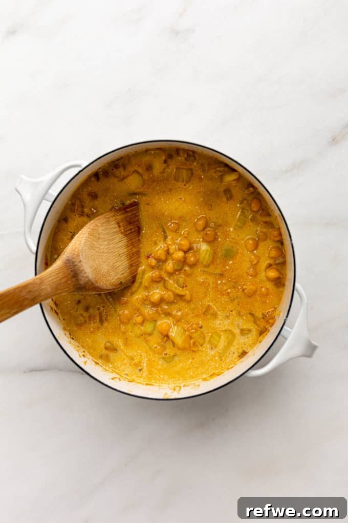 Creamy Coconut Chickpea Stew 8 Coconut curry chickpeas simmering in a pot, being mixed with a wooden spoon.