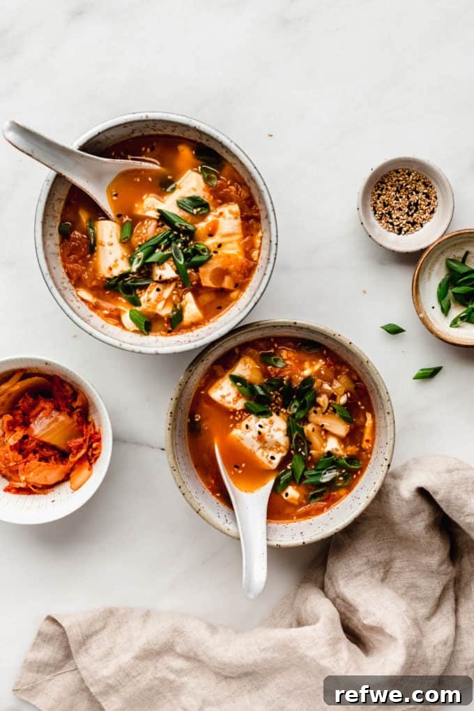 Spicy Korean Soft Tofu Stew 8 two bowl of kimchi soup with a side of kimchi, sesame seeds and green onions