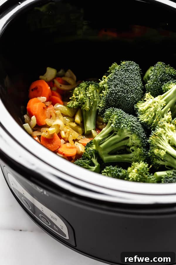 Assorted fresh broccoli florets and sautéed vegetables neatly arranged within a slow cooker, ready for cooking.