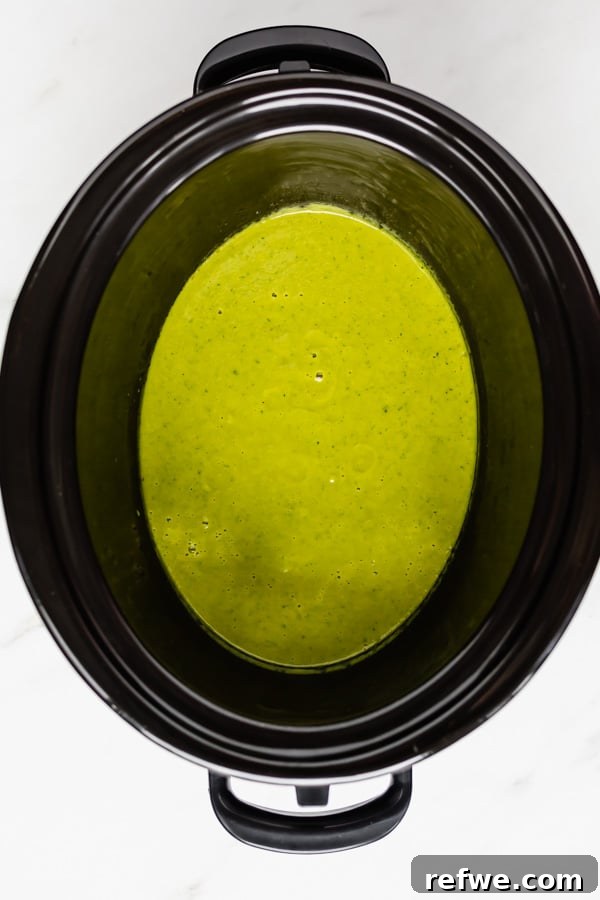 A vibrant green broccoli soup, still chunky before blending, simmering in a slow cooker.