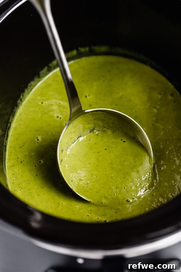 A ladle gently scoops a serving of creamy broccoli soup from the slow cooker, showcasing its smooth texture.