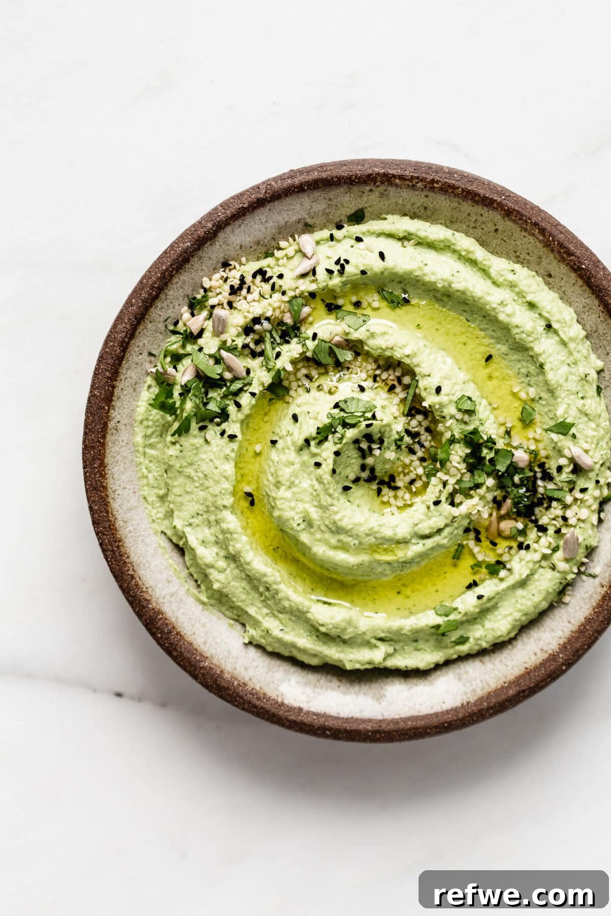 A small bowl of creamy green edamame hummus, garnished with olive oil and seeds.