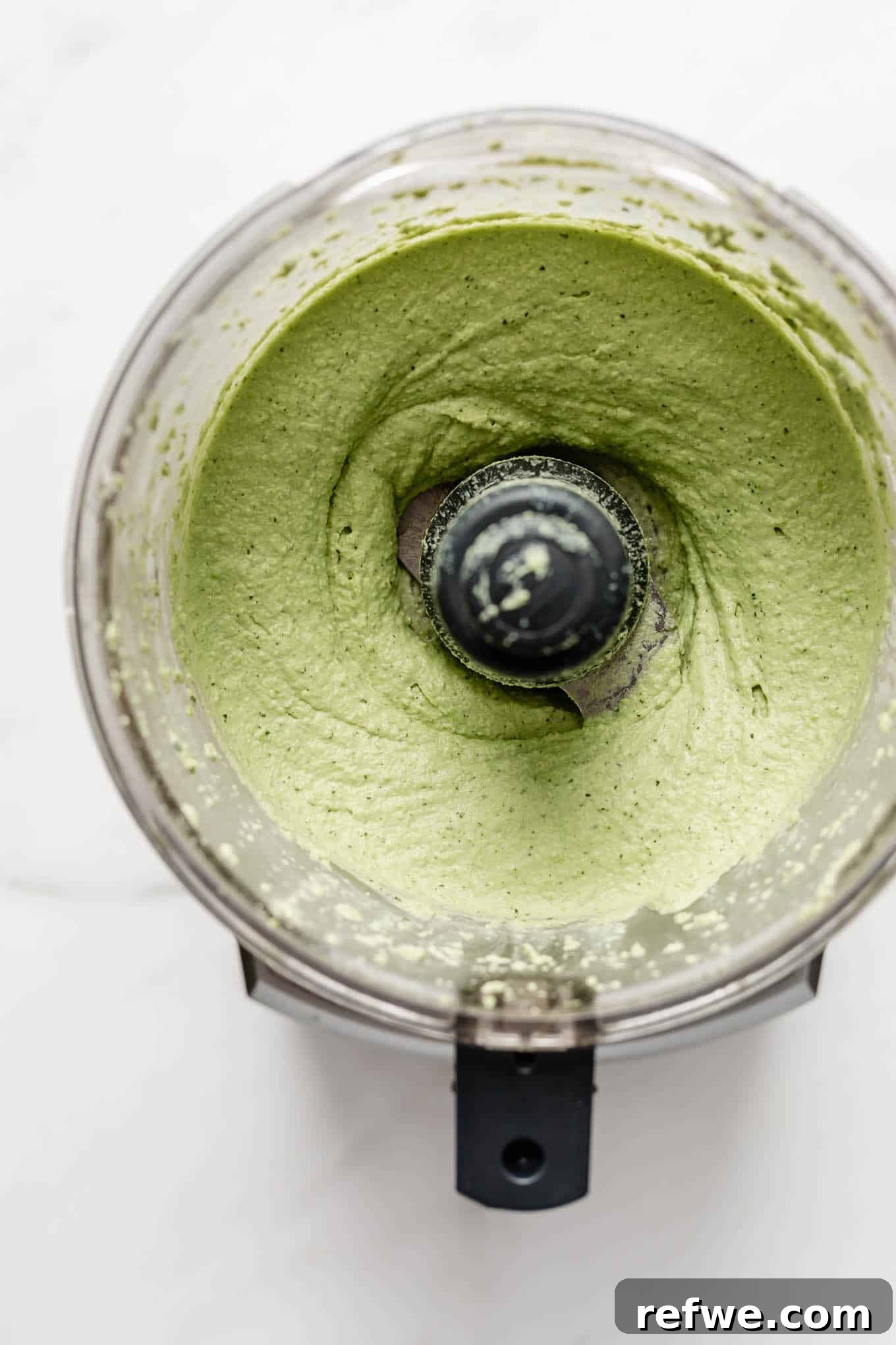 Creamy green edamame hummus swirling in a food processor bowl, indicating it's almost ready.