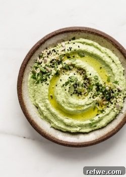 Edamame hummus topped with olive oil, seeds and chopped cilantro on a brown ceramic plate