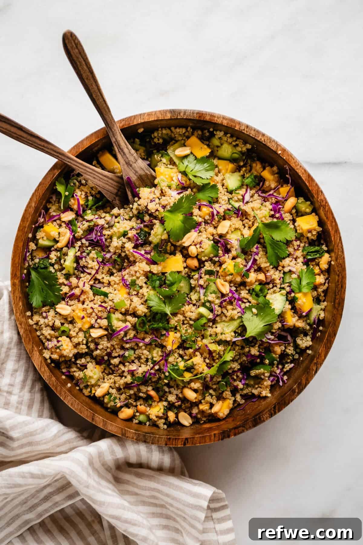 Thai Peanut Quinoa Bowl 2 A vibrant Thai quinoa salad in a rustic wood salad bowl, accompanied by elegant wooden serving spoons, ready to be enjoyed.