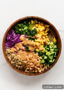 A beautifully presented Thai quinoa salad, generously dressed with creamy peanut sauce, in a stylish wood salad bowl, ready to be served.