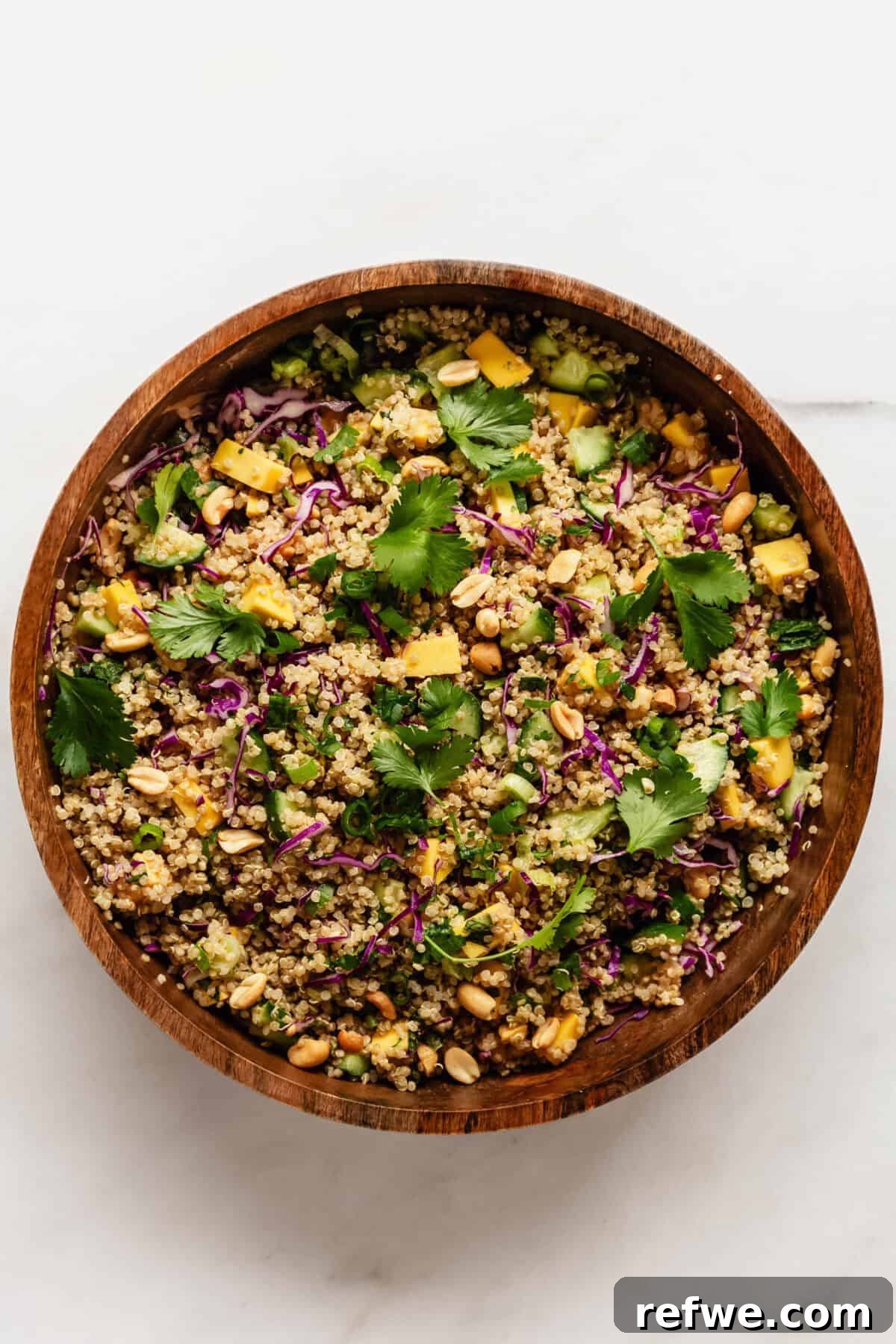 Thai Peanut Quinoa Bowl 8 The Thai quinoa salad, now thoroughly mixed with the peanut dressing and garnished with fresh cilantro leaves, is presented in a beautiful wood mixing bowl, ready to be served and enjoyed.