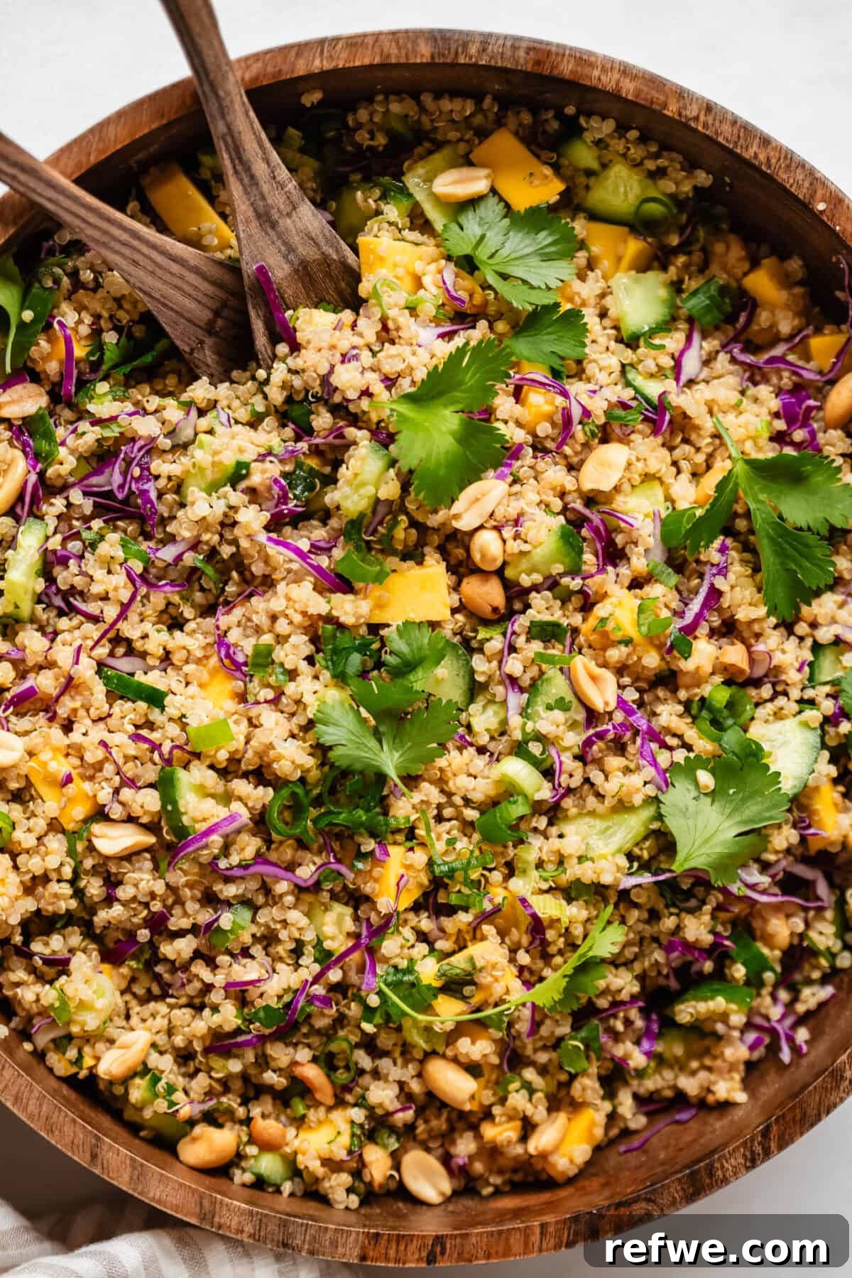 Thai Peanut Quinoa Bowl 9 A close-up of a perfectly mixed quinoa salad featuring sweet mango, crisp cucumber, vibrant scallions, and fresh cilantro, generously coated in peanut dressing, presented in an elegant wood salad bowl.