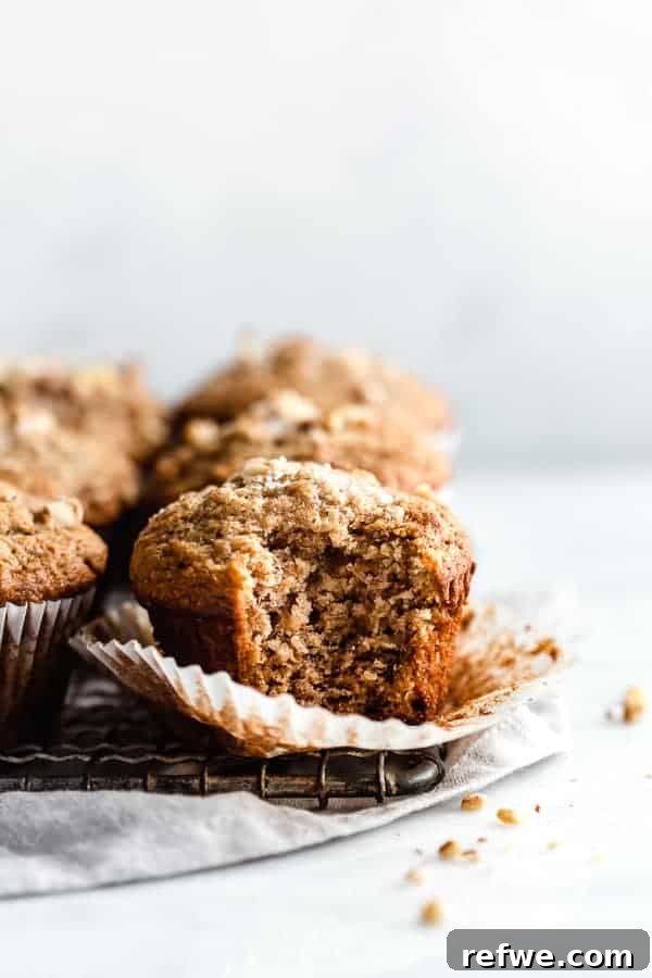 Quick Nutritious Morning Meals 16 cooling rack filled with healthy breakfast banana nut muffins, with a bite taken out of one muffin on top of a grey linen