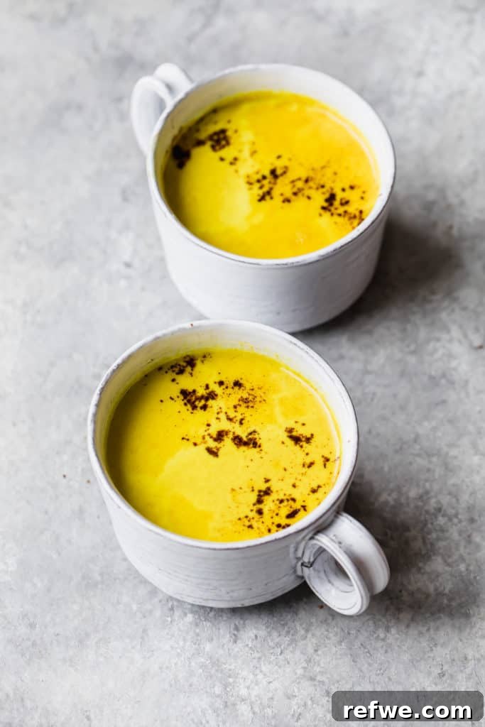 Quick Nutritious Morning Meals 18 two white mugs filled with yellow turmeric latte and topped with cinnamon, on a grey background