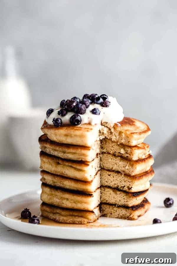 Quick Nutritious Morning Meals 4 healthy breakfast pancakes topped with cream and blueberries, on a white plate against a grey background