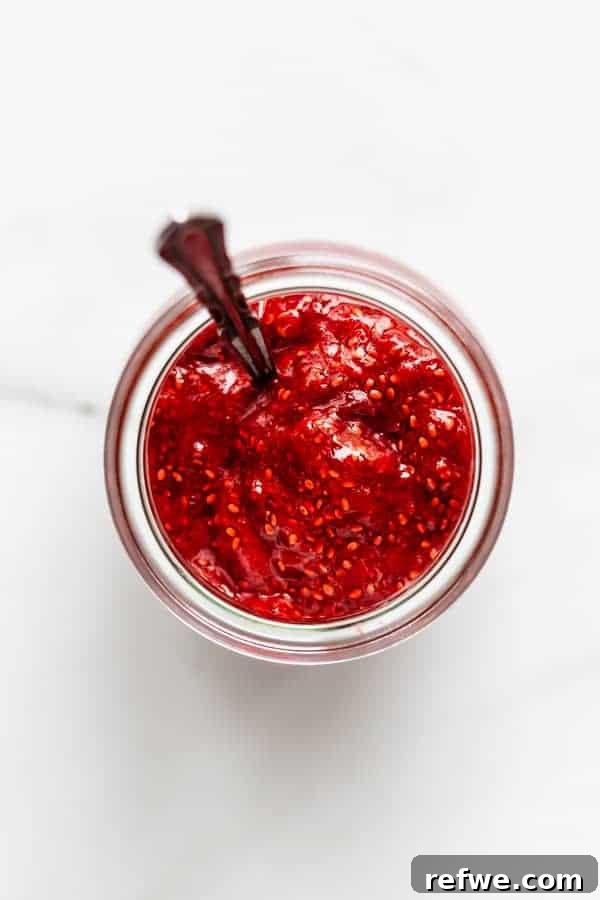 Quick Nutritious Morning Meals 5 silver spoon sitting in a glass jar filled with strawberry chia jam on a marble counter