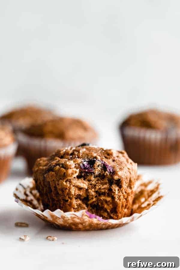 Quick Nutritious Morning Meals 10 a healthy breakfast muffin with a bite taken out of it, on the muffin paper with blueberry muffins in the background