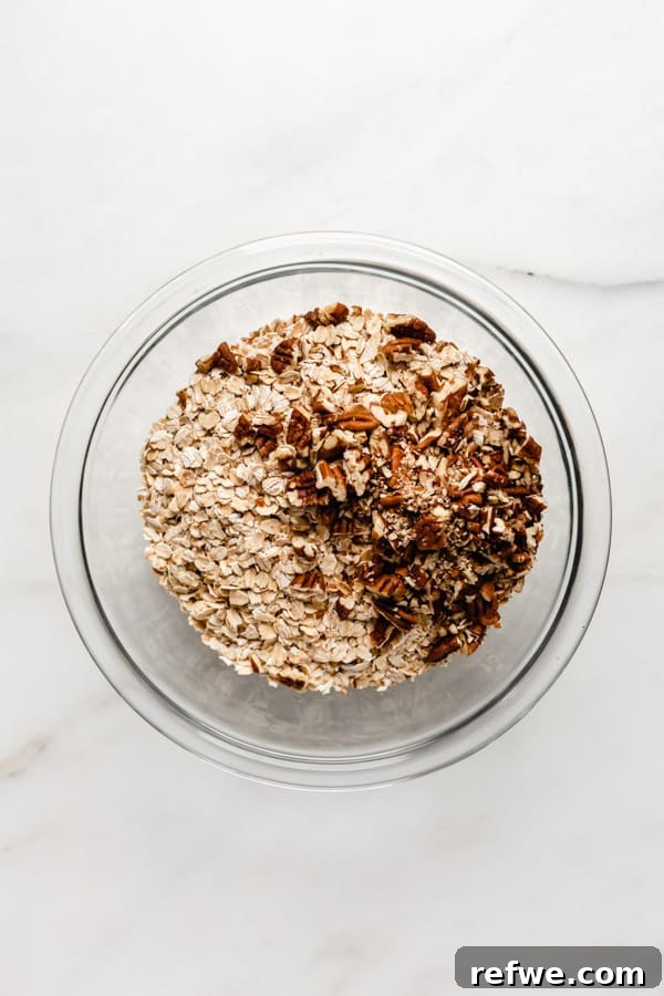 Spiced Banana Bread Granola 3 A clear mixing bowl holding a blend of rolled oats and chopped pecans, representing the dry ingredients for the granola.