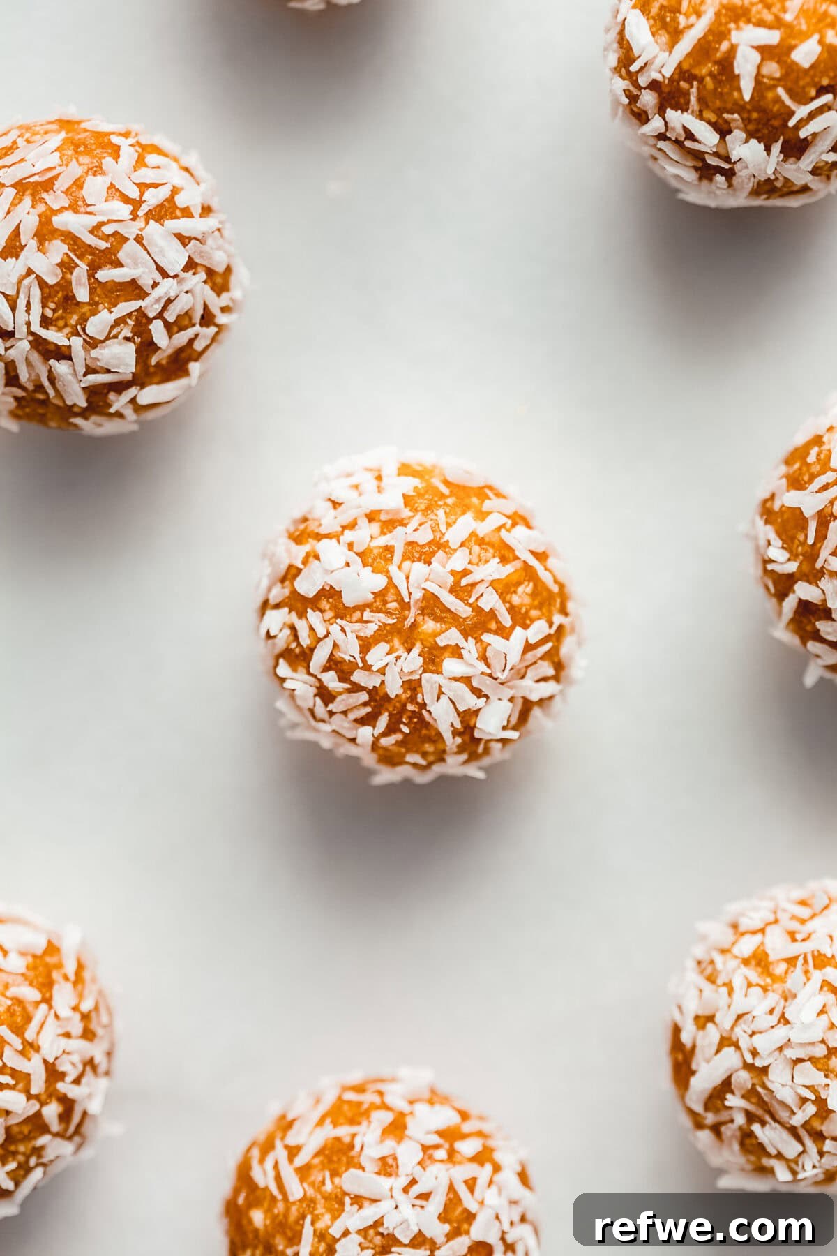 Sun Kissed Apricot Coconut Power Bites 6 Several apricot energy balls coated in shredded coconut, neatly arranged on a marble board, showcasing their appealing texture.