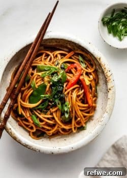 vegetable lo mein in a ceramic bowl with a side of sliced green onions