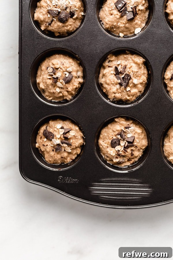Portable Oat Cups 7 A muffin pan filled with unbaked oatmeal cup batter, topped with chocolate and oats, ready for the oven.