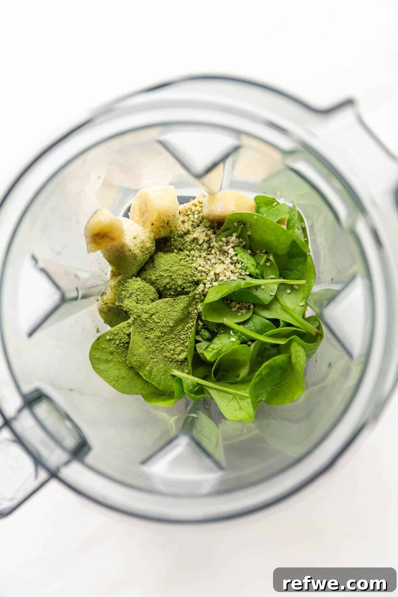 Vibrant Matcha Smoothie 4 A blender filled with fresh spinach, frozen mango, bananas, matcha powder, and hemp seeds, ready to be blended.